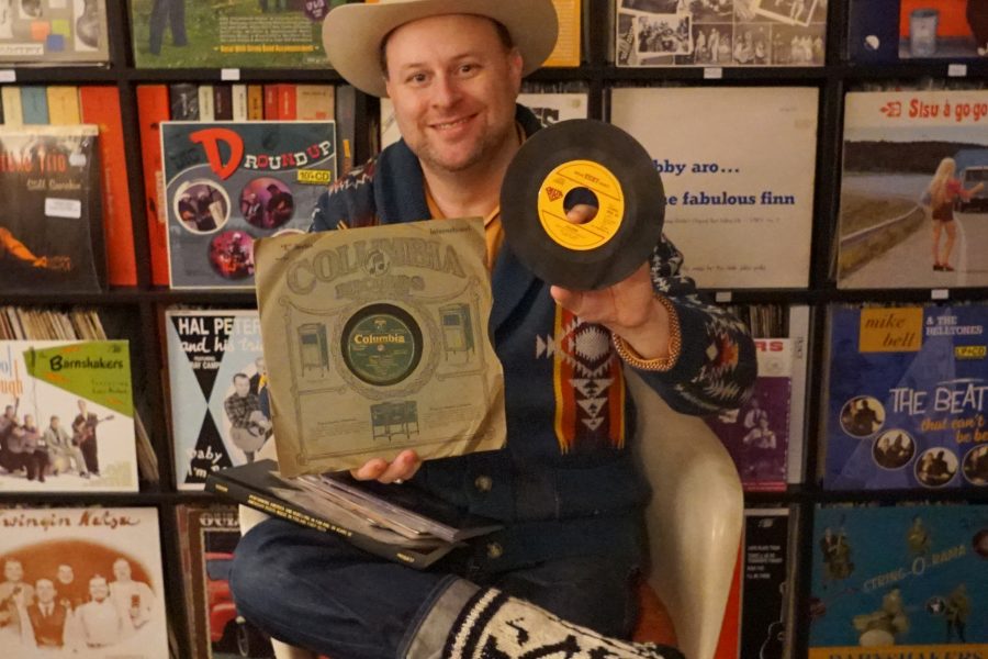 Nathan Gibson wearing a cowboy hat and cowboy boots poses with several country music records